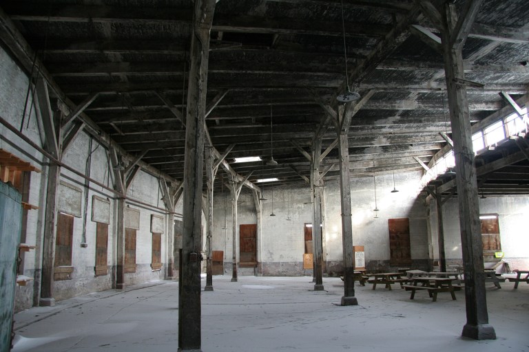 Interior of the Canadian Northern Railway Roundhouse, December 2013. The fan-shape of the building is evident in the curvature of the rear wall (to the left), the clerestory windows (at the right) and the arrangement of the ceiling supports and beams. Alberta Culture and Tourism, Government of Alberta. 