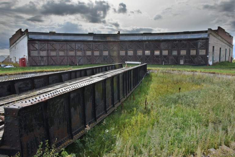 Exterior of the Canadian Northern Railway Roundhouse, showing the large, double doors, which provide access to the locomotive stalls. The turntable and bridge are in the foreground, September 2014. Alberta Culture and Tourism, Government of Alberta. 