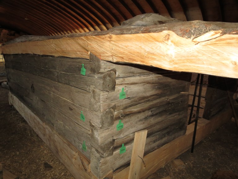 Reassembly of the Spring House using tags to retain the original log sequence, with seasoned new timber scribed, cut and tooled to match the historic construction of squared logs with half-dovetail joints. Although each joint is uniquely fitted to the adjacent logs, elements from the disassembled structure relaxed and made reassembly with the original logs more challenging. Source: JJD Contracting Ltd.