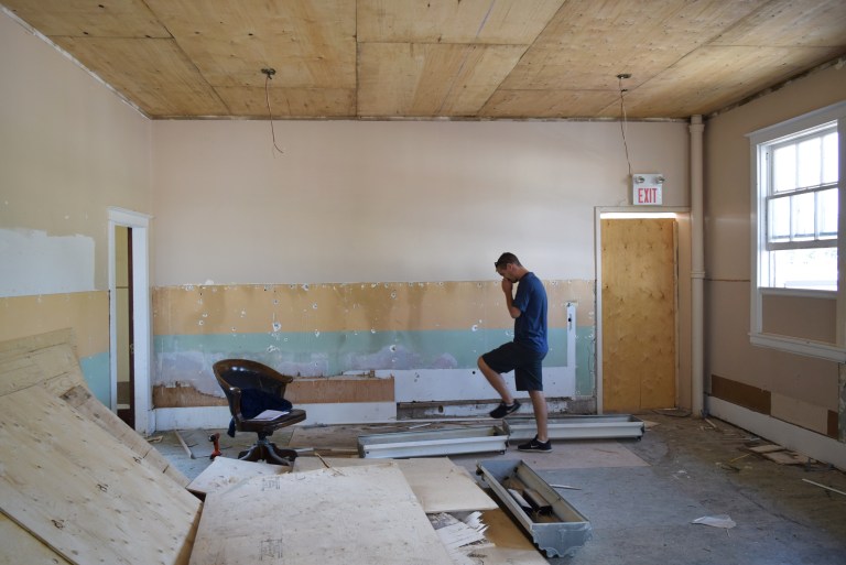 The former courtroom retains the original painted plaster walls after the removal of 1950s plywood wainscot from the main floor. The wainscot represents the building’s later history as a municipal office. The wainscot was removed to restore the plaster interior from the period associated with the 1918 courthouse. Plywood on the ceiling covered plaster damage from roof leaks and supported mid-century acoustic tiles that have just been removed in this image. Source: Historic Resources Management Branch.
