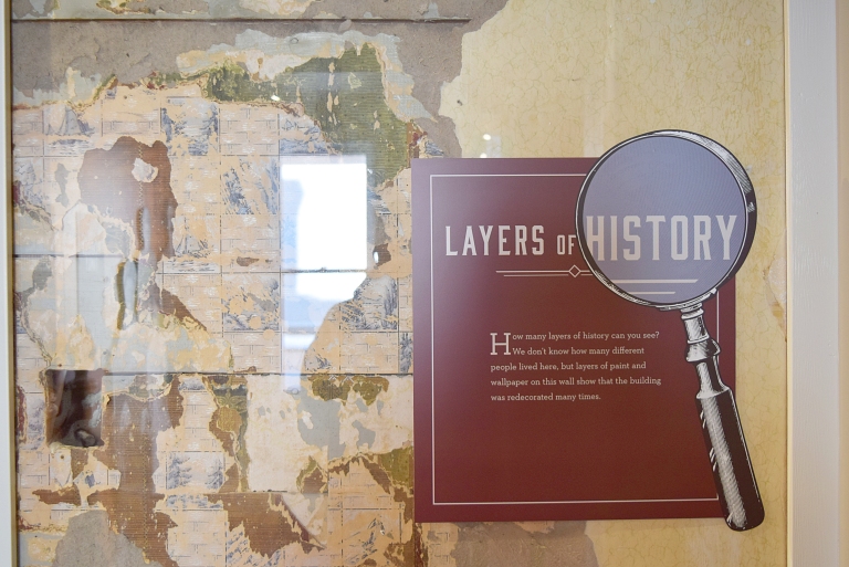An exhibit reveals the mosaic of historic wallpaper and other finishes preserved within the drywall interior. 